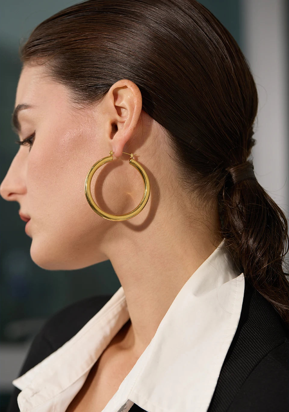 Close-up of a woman wearing gold hoop earrings with a blurred background
