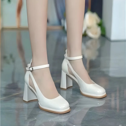 White high-heeled shoes with brown soles on a reflective surface.