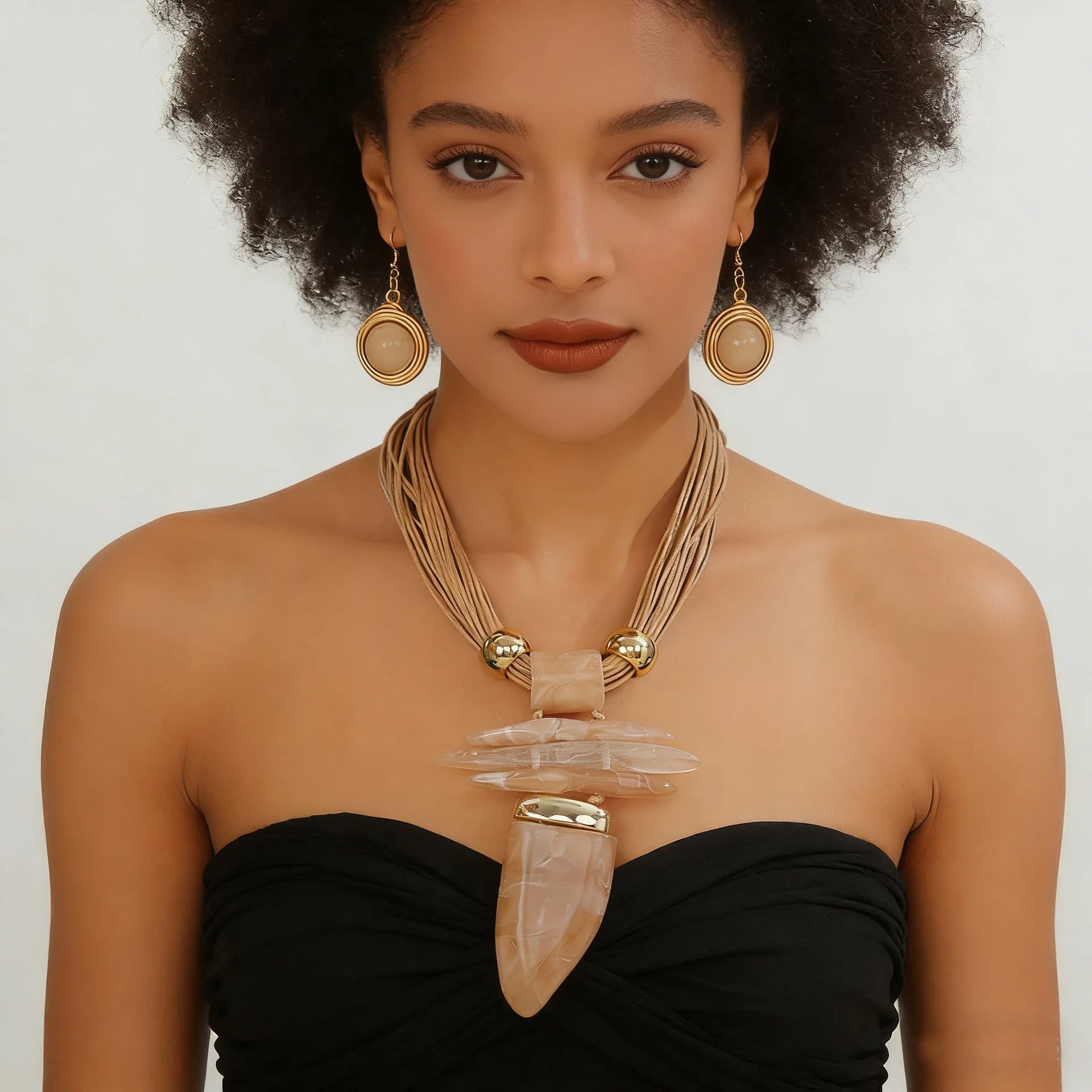 Woman wearing a black strapless top with a large necklace and gold earrings on a plain background