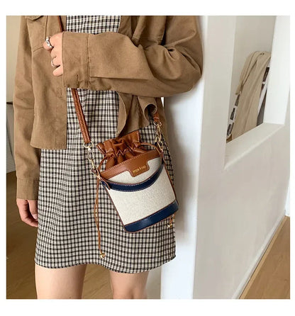 Person wearing a plaid skirt and brown jacket with a two-tone handbag.