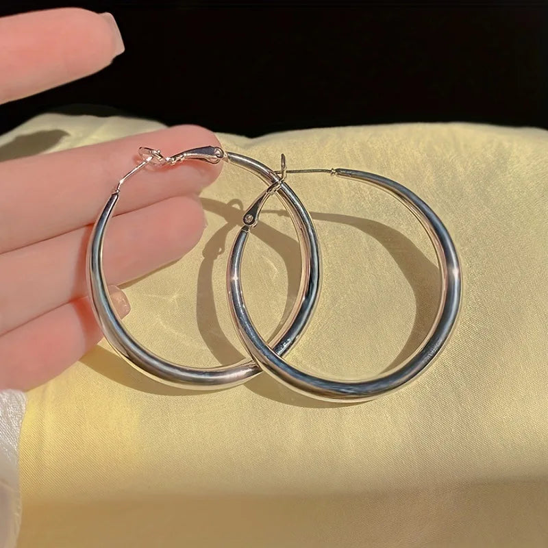 Silver hoop earrings held by a hand on a yellow fabric background