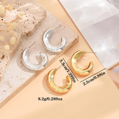 Gold and silver crescent-shaped earrings on a beige surface with measurements.
