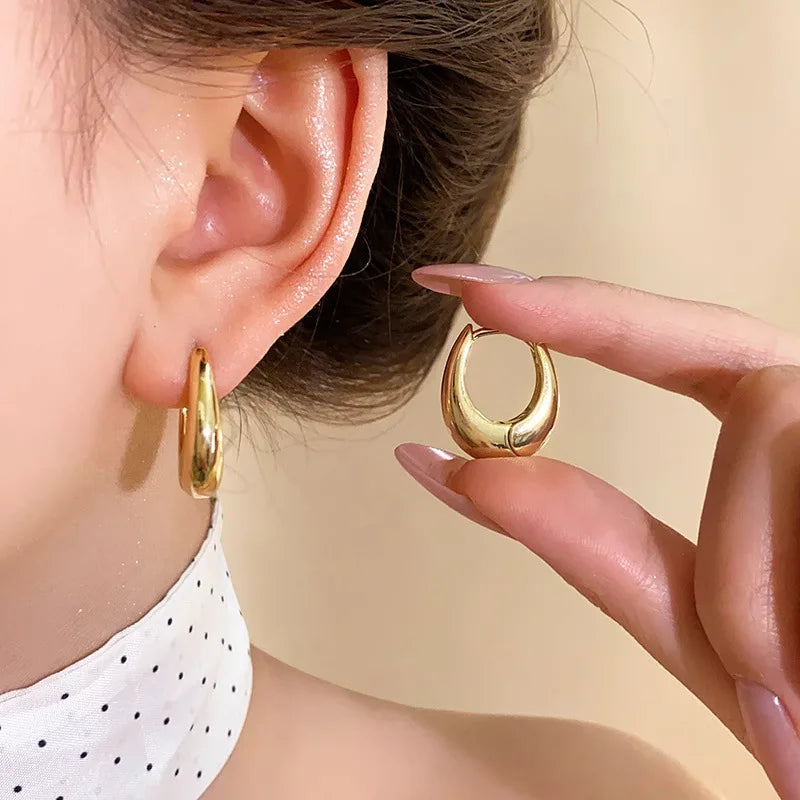 Gold hoop earrings being worn and held up to an ear against a neutral background