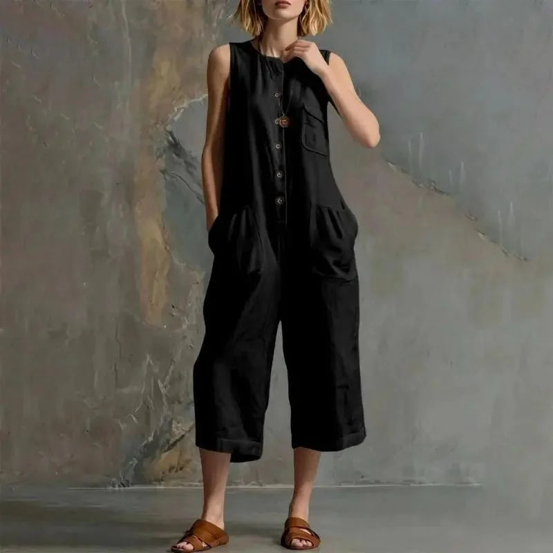 Person wearing a black sleeveless jumpsuit against a textured wall.