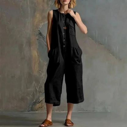 Person wearing a black sleeveless jumpsuit against a textured wall.