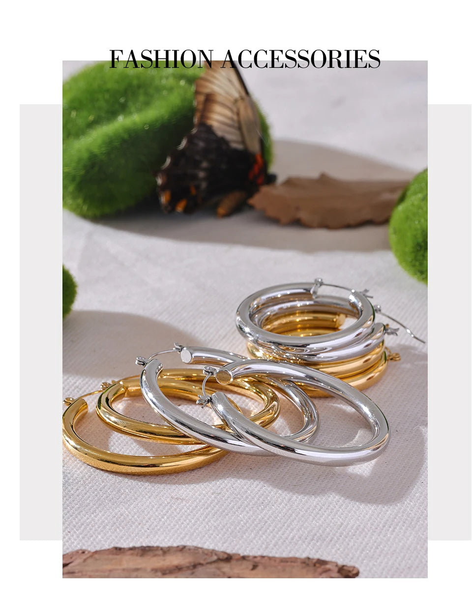Gold and silver hoop earrings on a textured surface with a butterfly in the background.