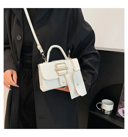 Person holding a white handbag with gold accents, wearing a black coat indoors.