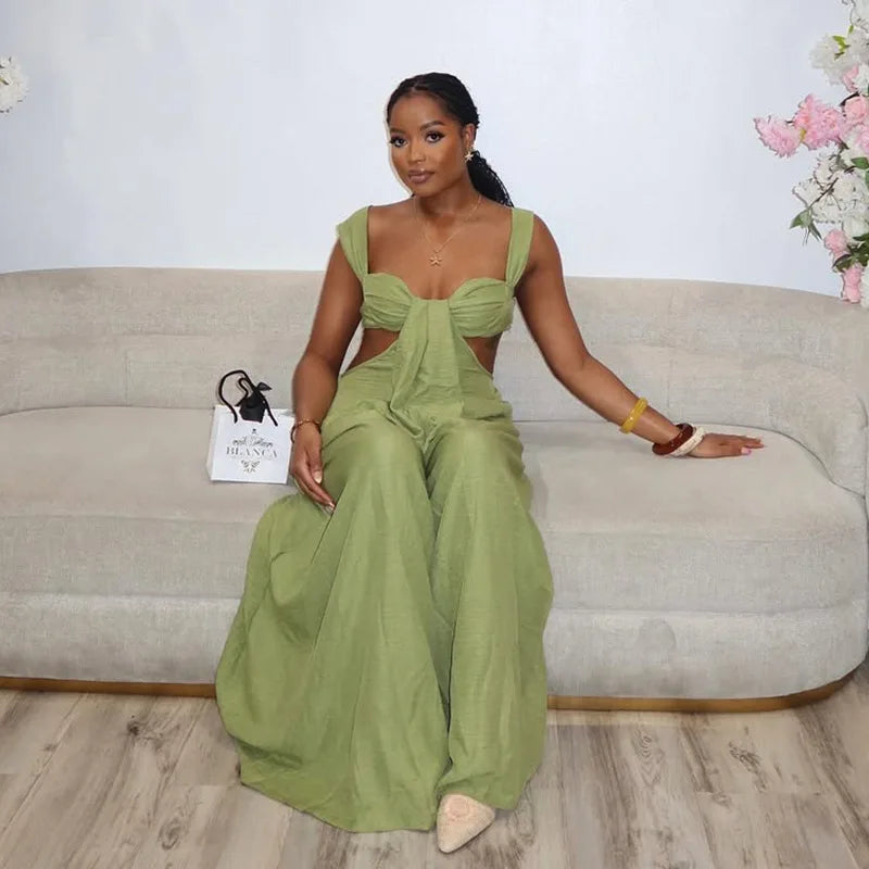 Woman in a green dress sitting on a beige couch with a white wall and floral decorations in the background.