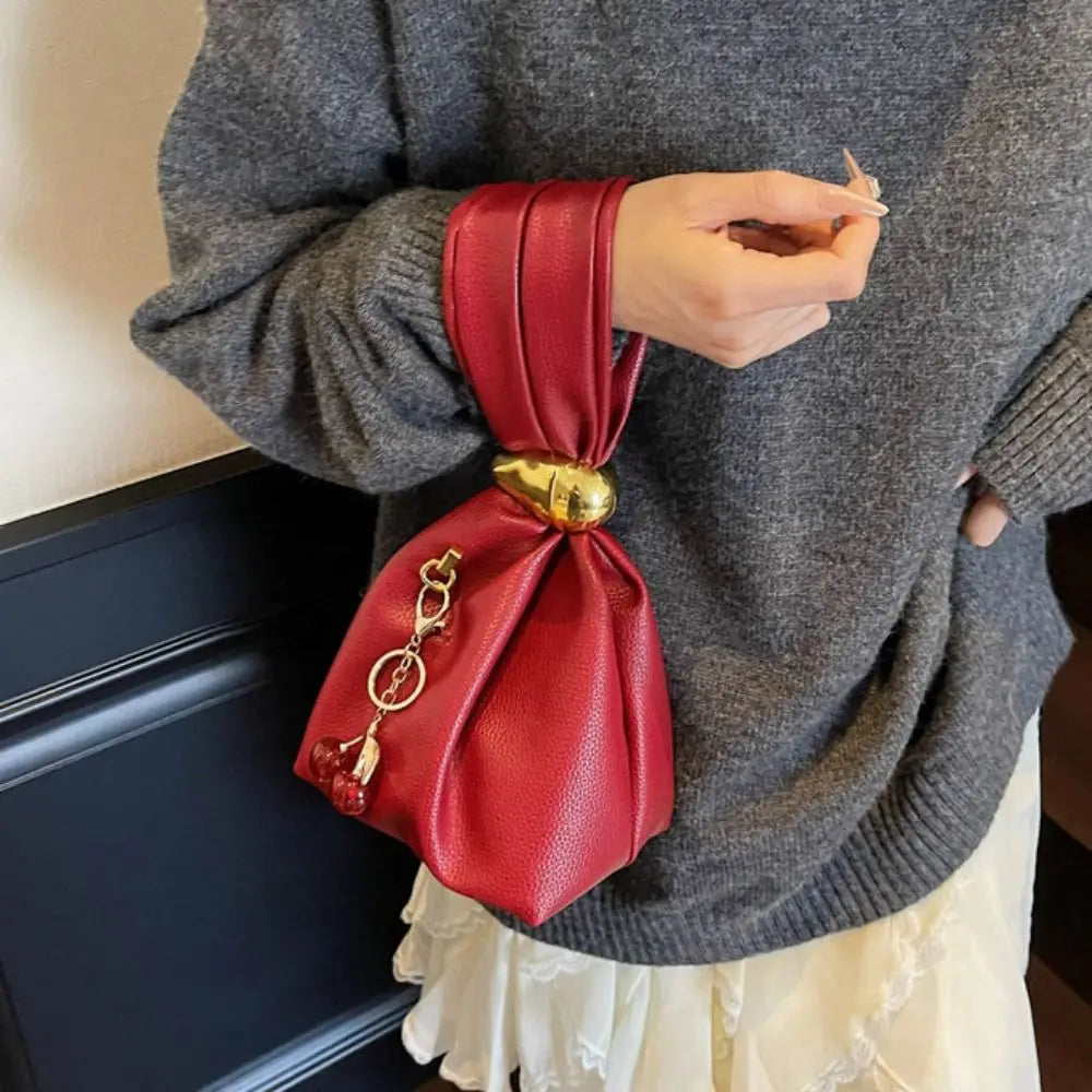 Person holding a red leather bag with a gold clasp against a neutral background