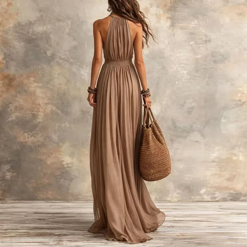 Woman in a long brown dress holding a woven bag against a textured wall.