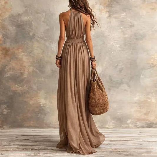 Woman in a long brown dress holding a woven bag against a textured wall.