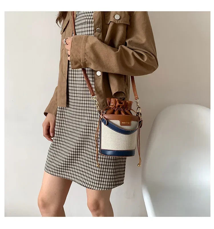 Person wearing a plaid skirt and brown jacket holding a bucket bag with a neutral background