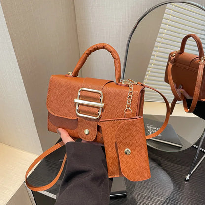 Brown leather handbag with gold buckle held by a person, mirror reflection visible.