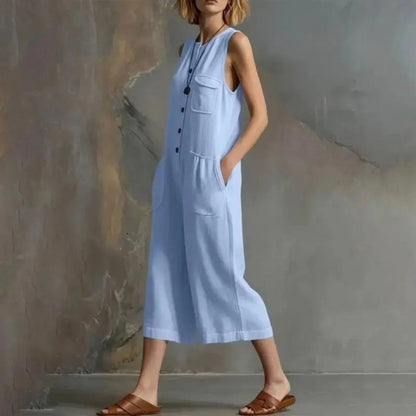 Woman wearing a light blue sleeveless jumpsuit against a textured wall.