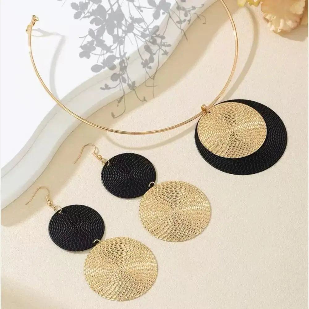 Gold and black circular earrings on a white surface with a blurred background