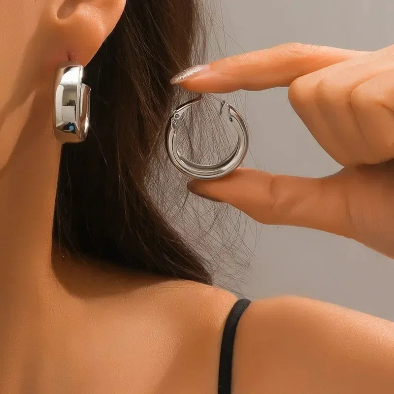 Close-up of a person wearing a silver hoop earring with another hand pointing to it.