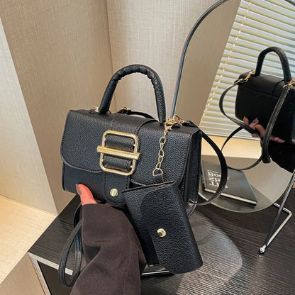 Black handbag with gold accents held by a person, reflected in a mirror.