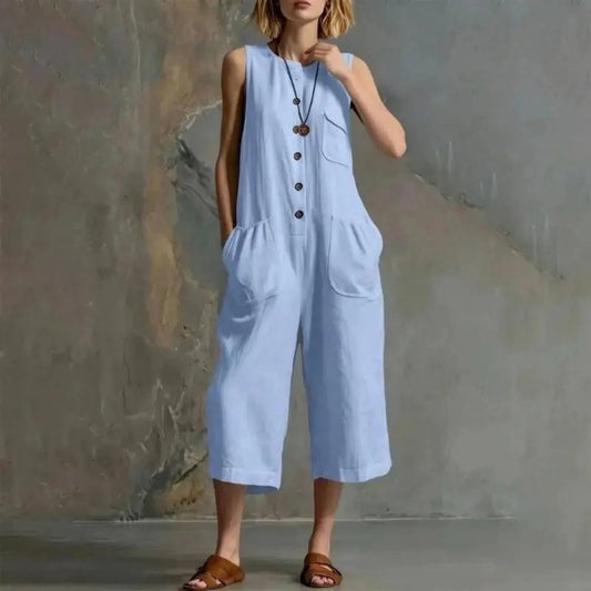 A woman models a light blue sleeveless wide-leg jumpsuit with front pockets and a button placket, standing against a textured gray wall. The brand name 'XJGOOD' is printed in black in the top left corner.