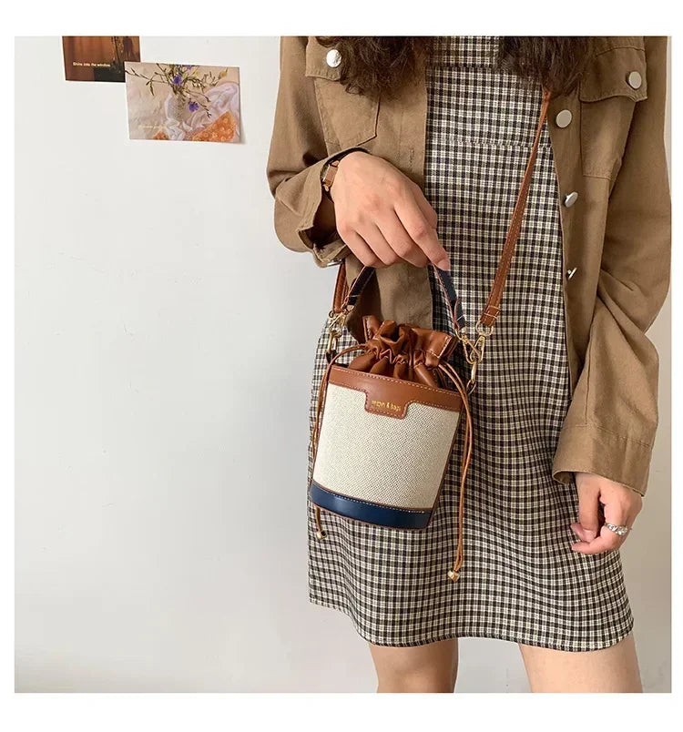 Person holding a drawstring bag with a plaid skirt and beige jacket against a white background