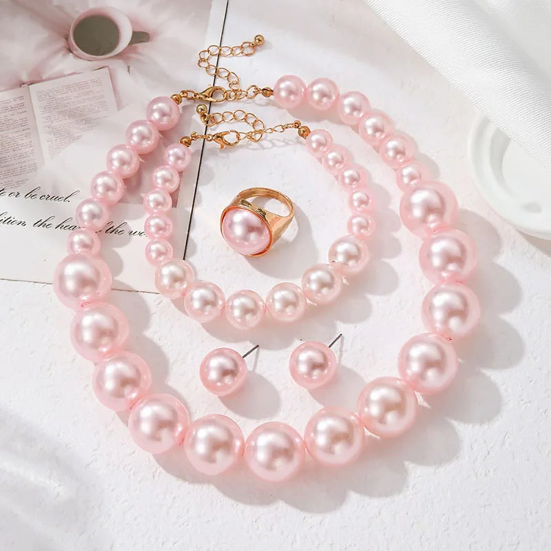 Pink pearl necklace, bracelet, and ring on a white surface with a book underneath.