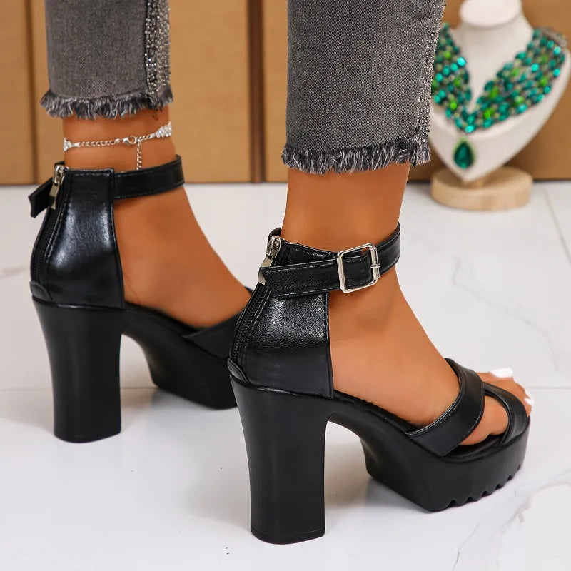 Black high-heeled sandals worn with gray jeans on a white surface.