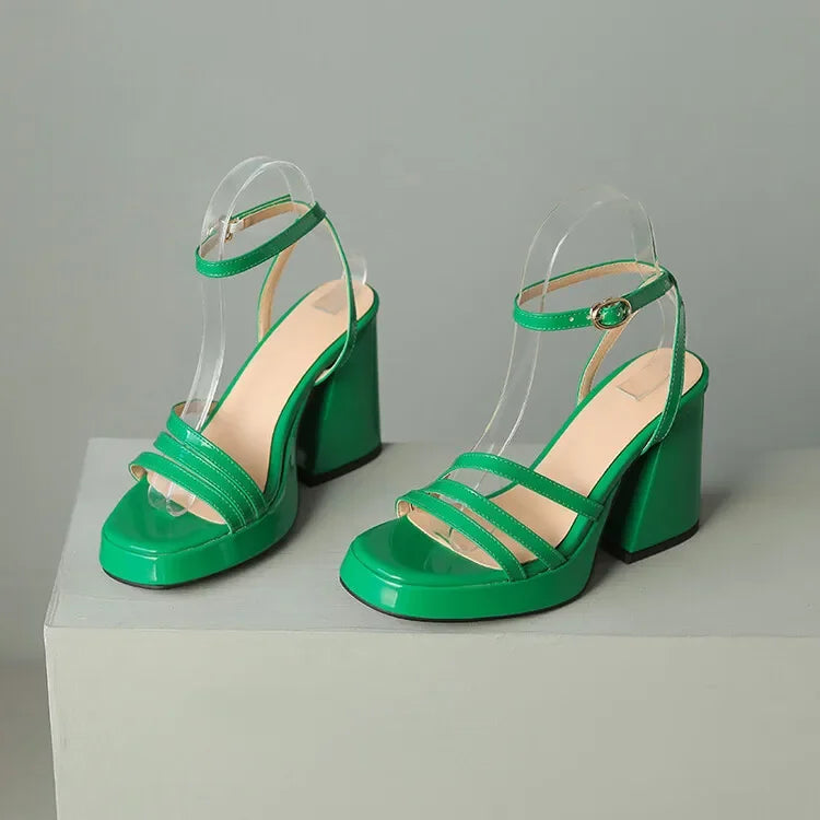 Green high-heeled sandals on a white platform with a gray background