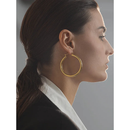 Woman wearing gold hoop earrings with a neutral background
