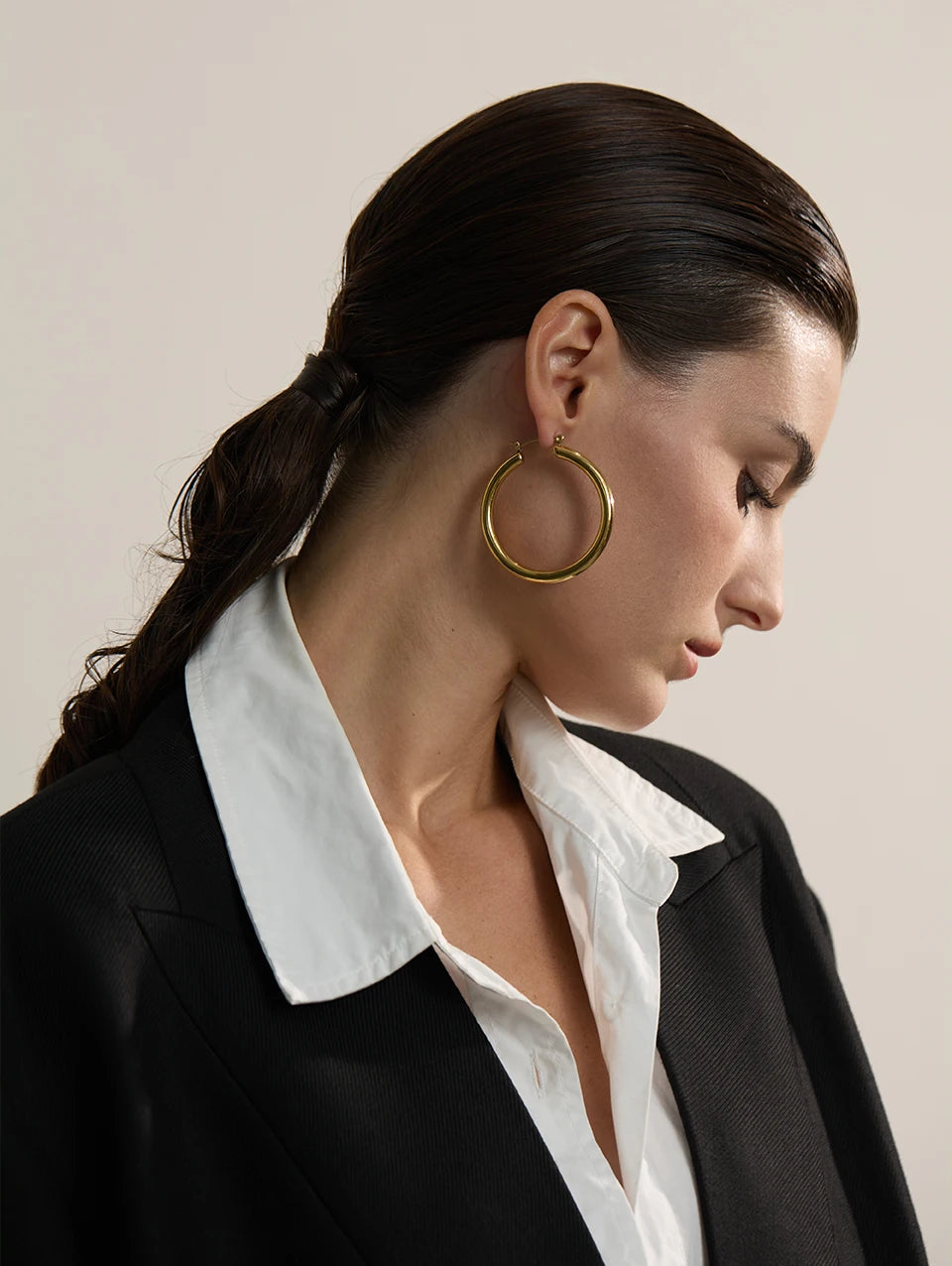 Woman wearing a gold hoop earring with a neutral background
