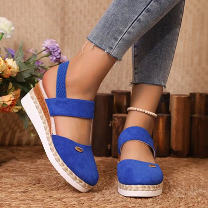 Blue sandals worn with jeans on a textured surface with flowers in the background