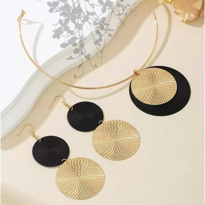 Gold and black circular earrings on a white surface with a blurred background