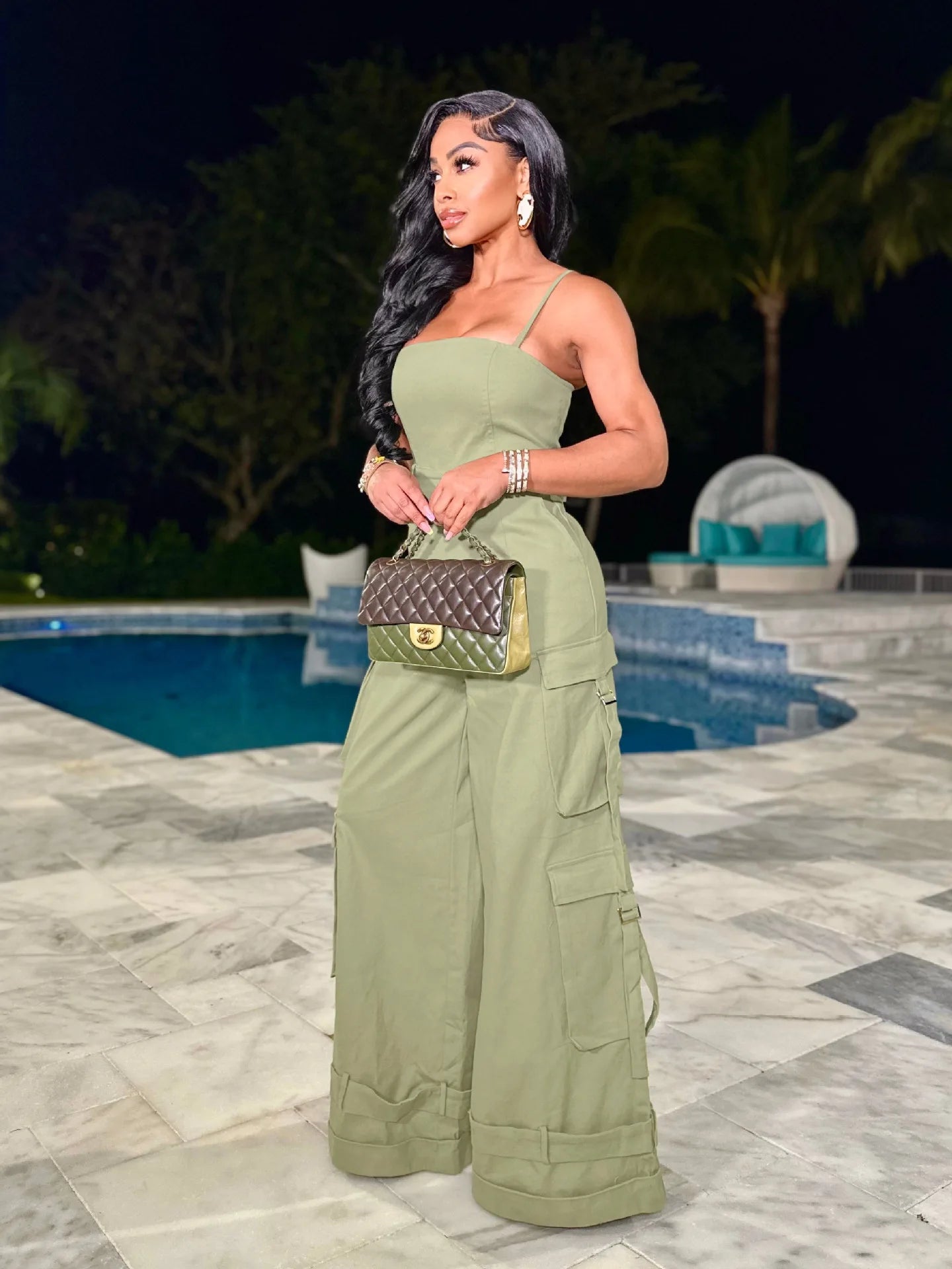 Woman in a green outfit standing by a pool at night