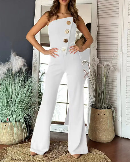 Woman wearing a white strapless jumpsuit with gold buttons in a room with plants.