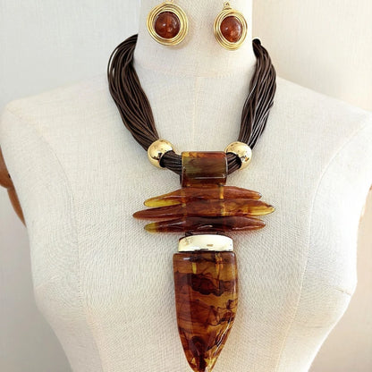 An amber and brown statement necklace displayed on a cream fabric mannequin torso, accompanied by matching amber and gold stud earrings.