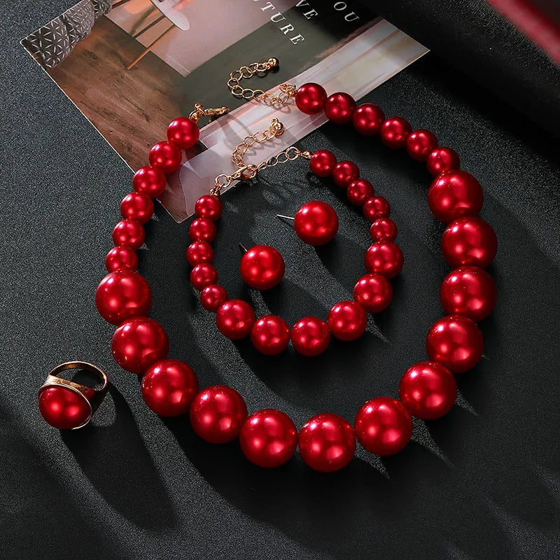 Red pearl necklace and earrings on a dark surface with a magazine underneath.