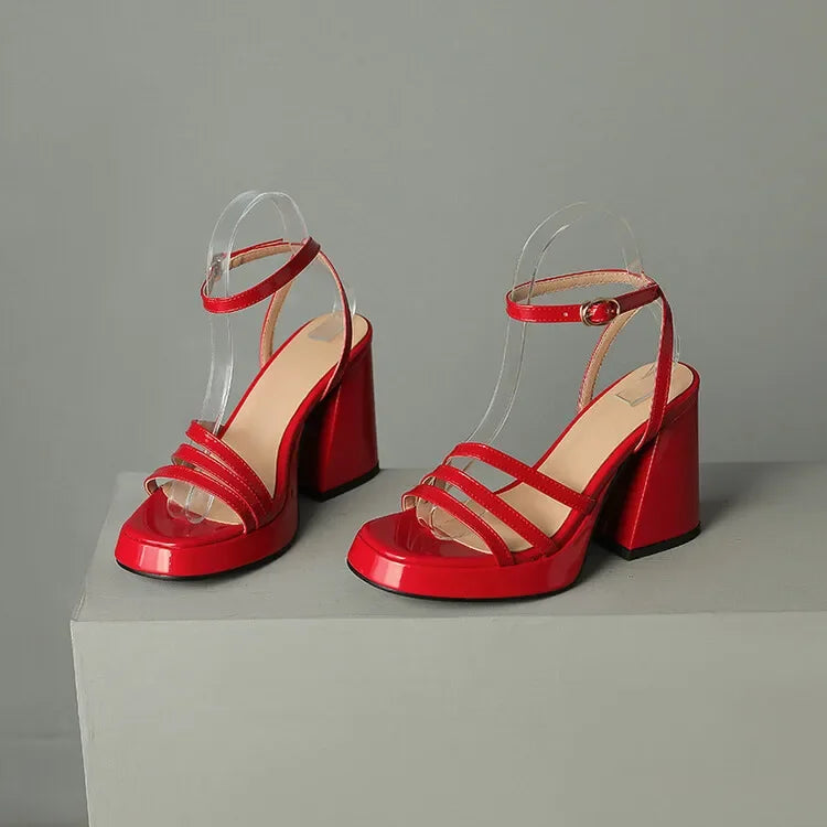 Red high-heeled sandals with clear straps on a gray background