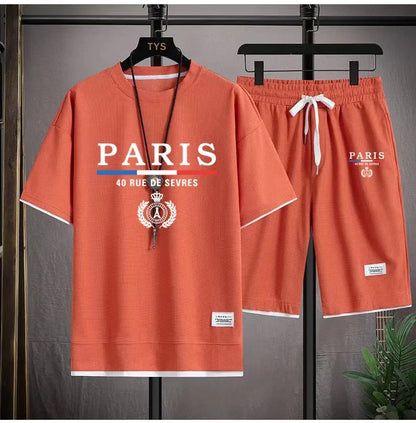 Orange t-shirt and shorts set with 'PARIS' branding on hangers against a gray background.