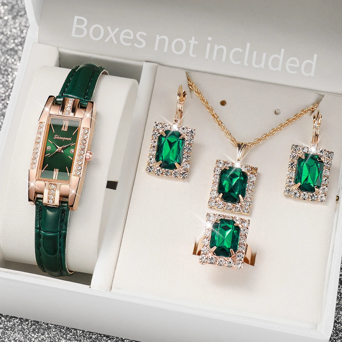 Jewelry set with green gemstones including a watch, necklace, and earrings on a gray surface.