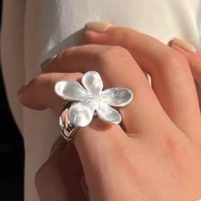 Silver flower-shaped ring on a hand with a blurred background