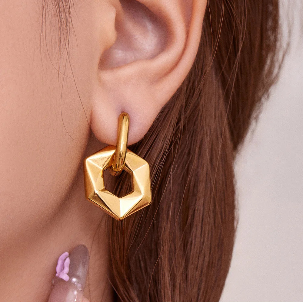 Gold geometric earring worn by a person with a neutral background