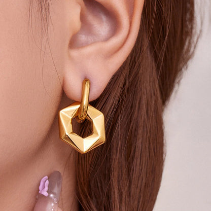 Gold geometric earring worn by a person with a neutral background