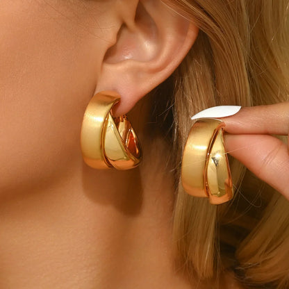 Gold hoop earrings being worn and adjusted by a person with blonde hair.