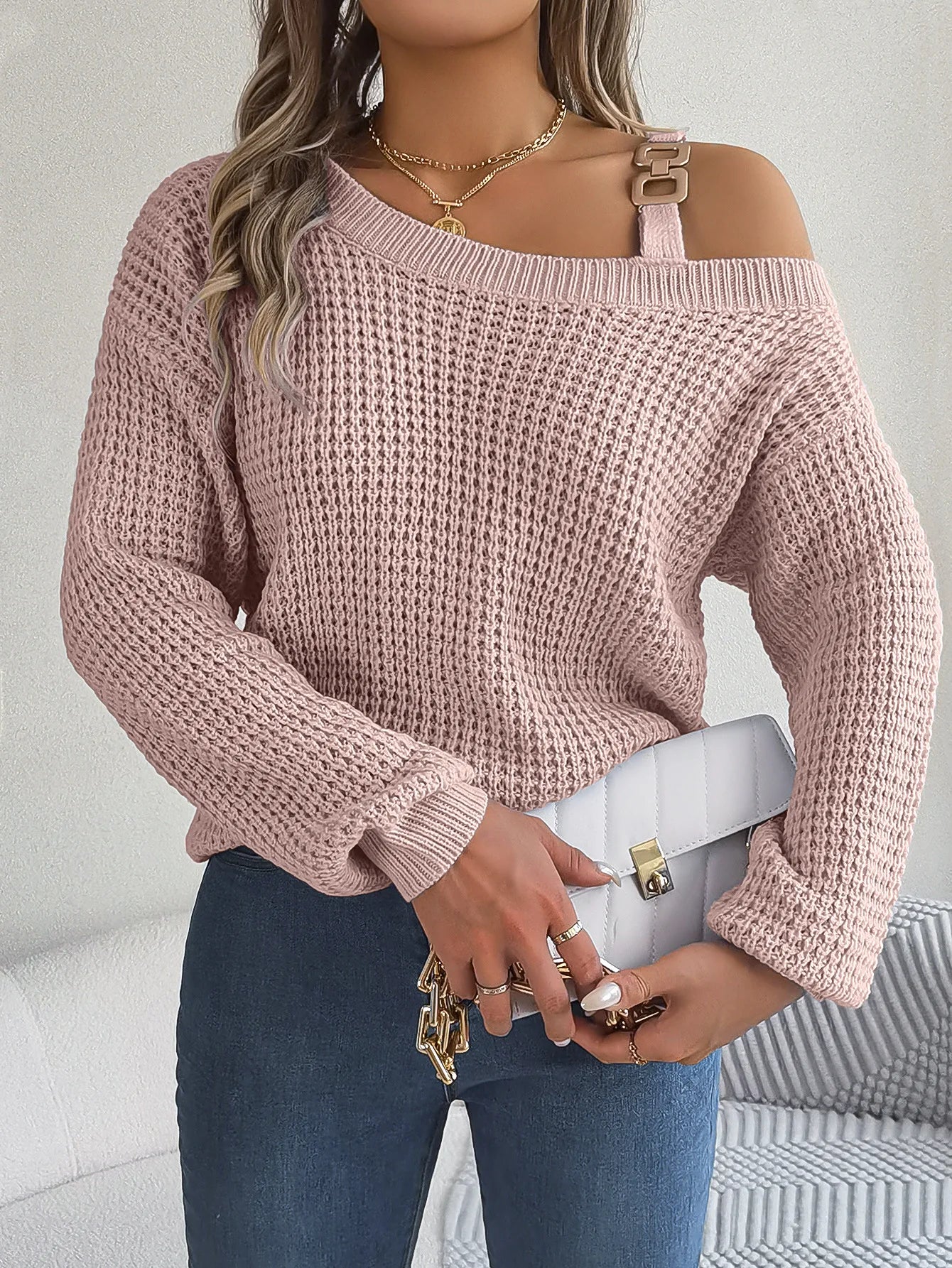 Person wearing a pink off-shoulder sweater holding a white handbag against a neutral background