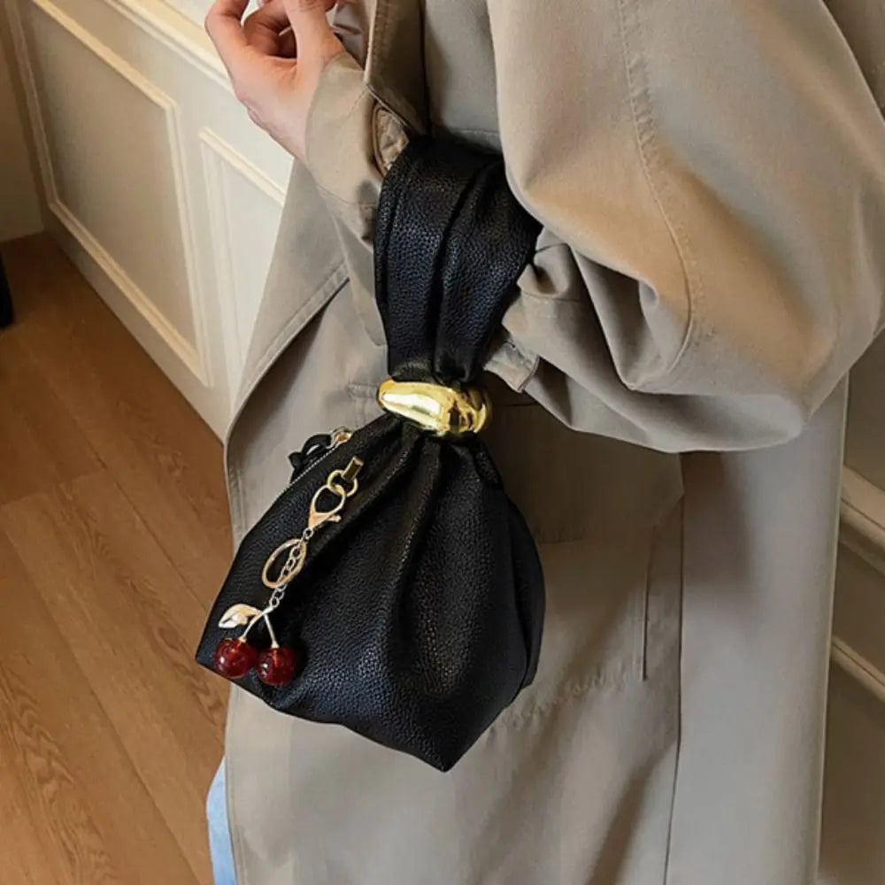 Person holding a black drawstring bag with cherry decorations against a neutral background