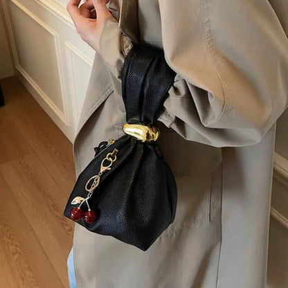 Person holding a black drawstring bag with cherry decorations against a neutral background