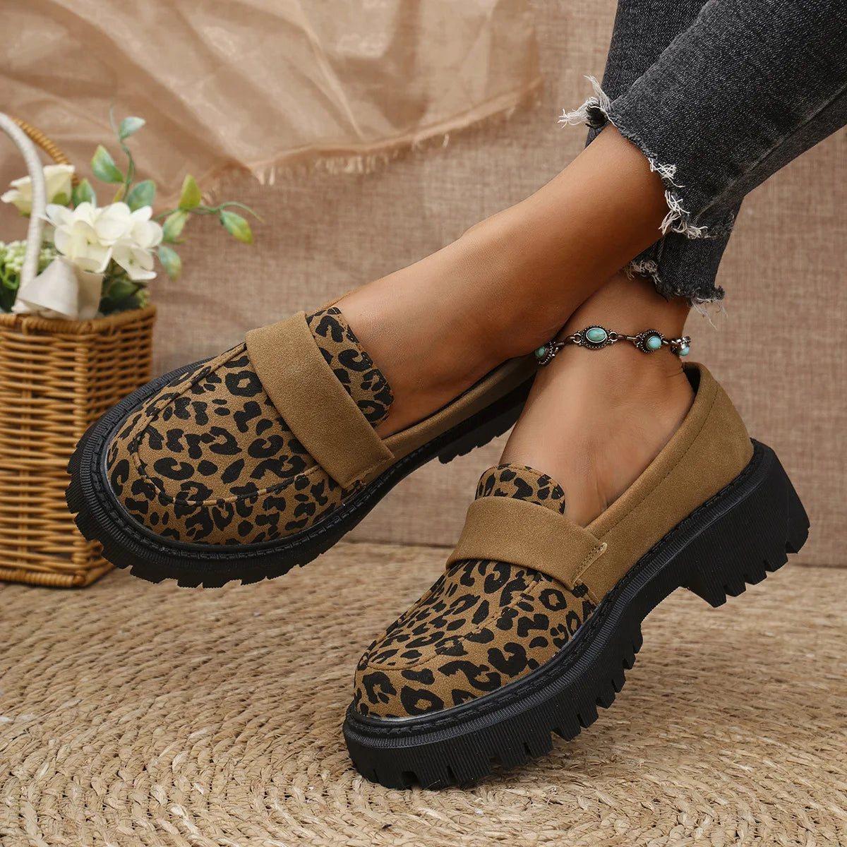 Leopard print shoes worn by a person on a textured surface with a basket of flowers in the background.