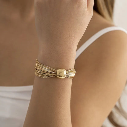 Gold-tone multi-strand chain bracelet with a smooth rounded centerpiece, shown on a woman's wrist with a white sleeveless top.