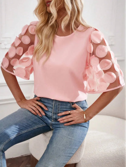 Woman wearing a pink blouse with sheer sleeves and blue jeans indoors.