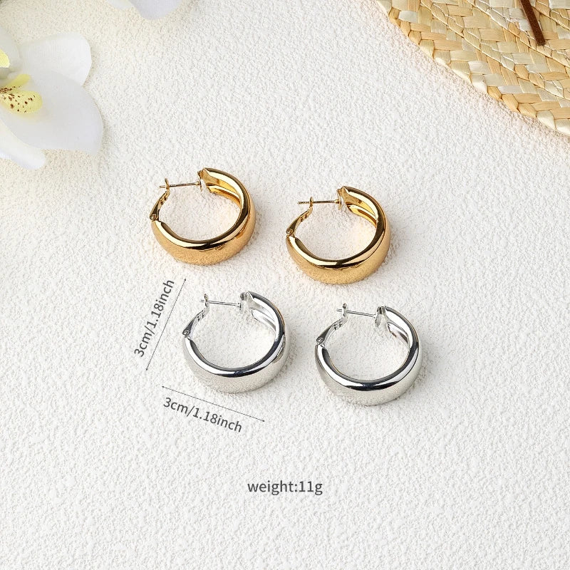 Two pairs of chunky hoop earrings shown on a textured white surface: one pair in polished gold and one pair in polished silver. Black measurement lines and text indicate 3cm/1.