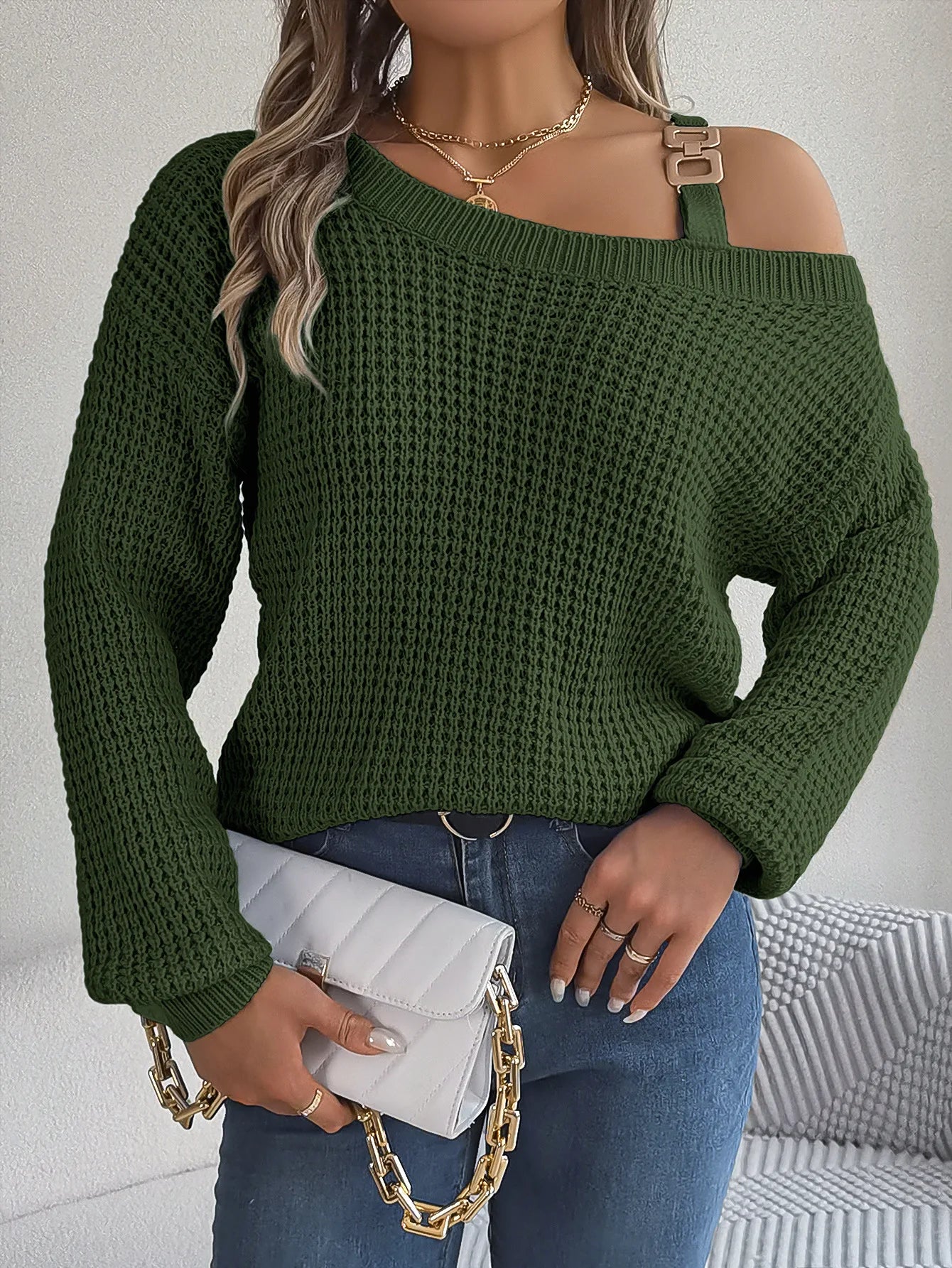Person wearing a green sweater with a white clutch and gold chain.
