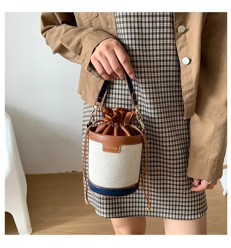 Person holding a drawstring bag with a plaid skirt and beige jacket.